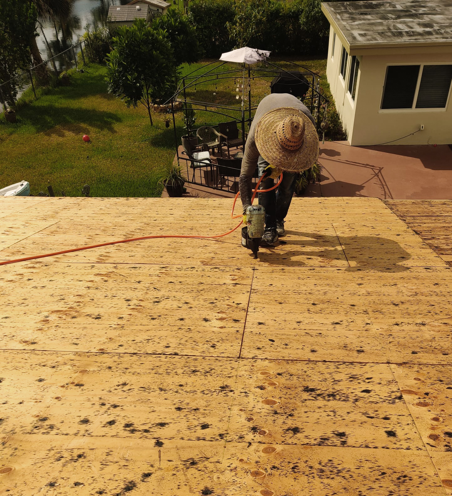 Worker on top of roof installing plywood to repair roof.
