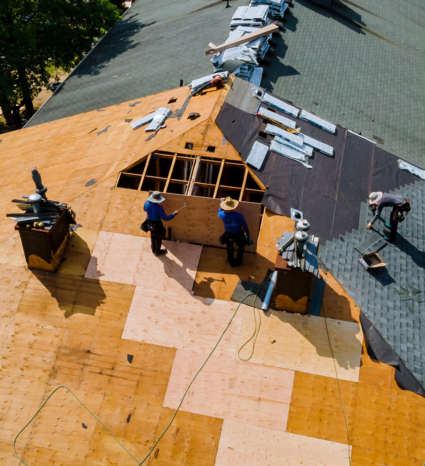 Three workers repairing the top of a roof.