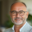 A bald latin man with glasses smiling.